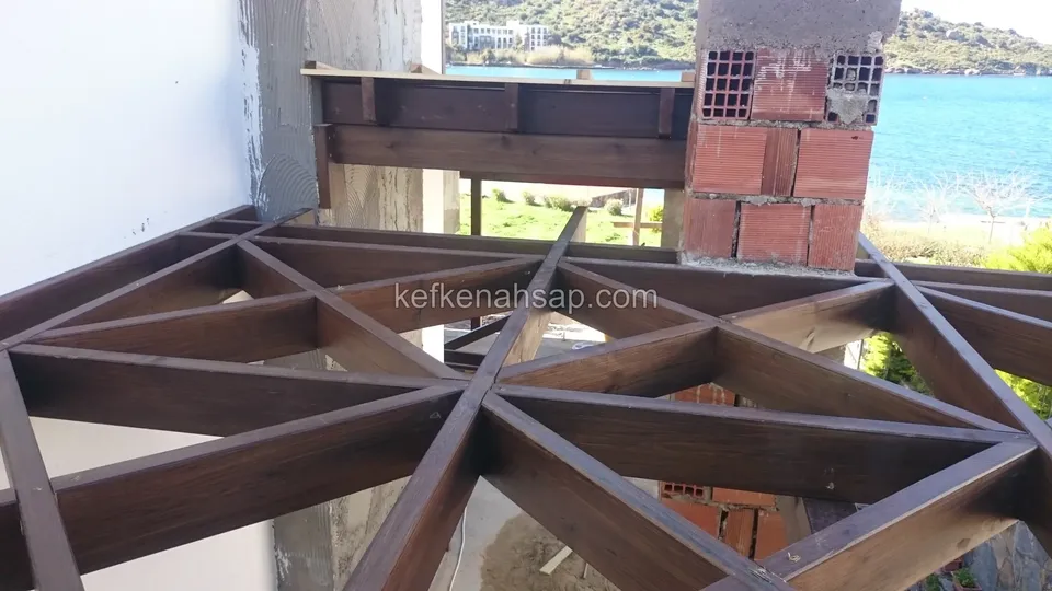 Tuğla kolon yanında üçgen desenli vernikli pergola kafesi, arkada teras ve mavi deniz