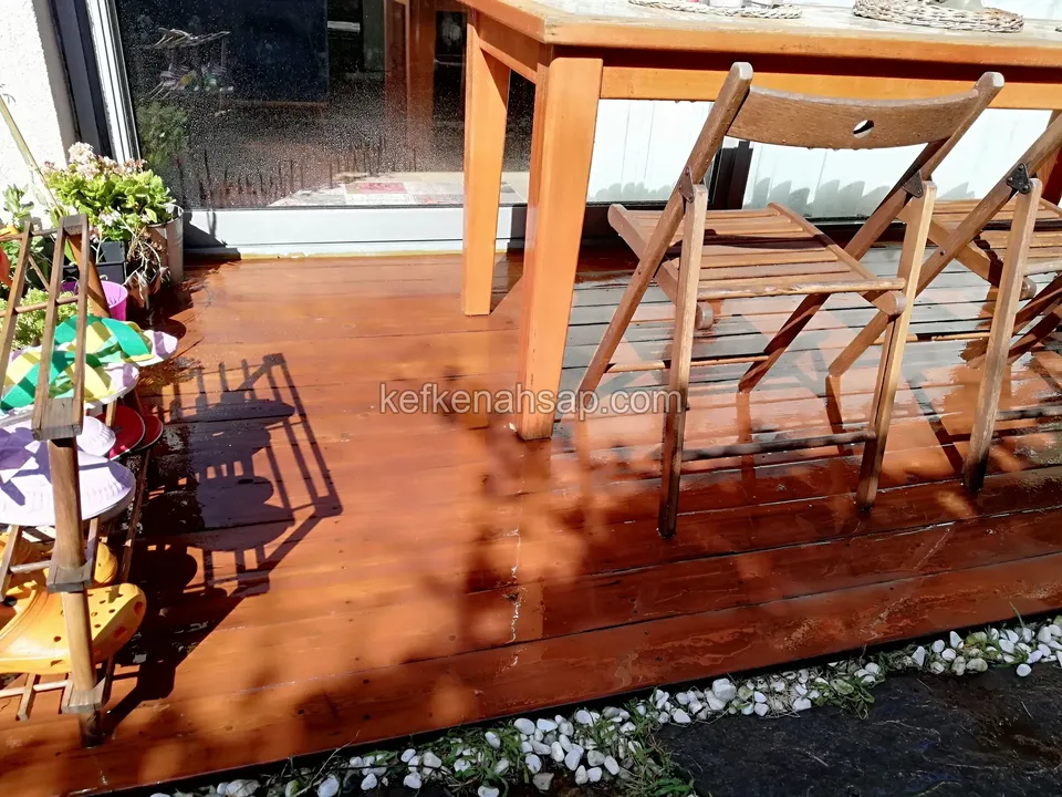 Timber table and folding chairs on an orange varnished deck, with white stones along the edge