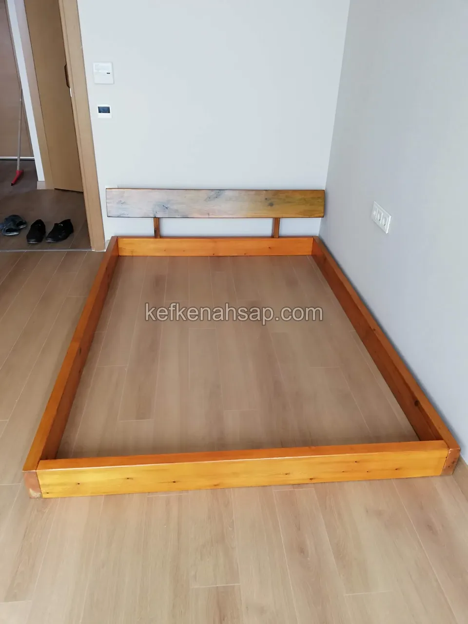 Parke zeminli odada, turuncu tonlu ahşap çerçeveli alçak yatak karkası ve ince başlık