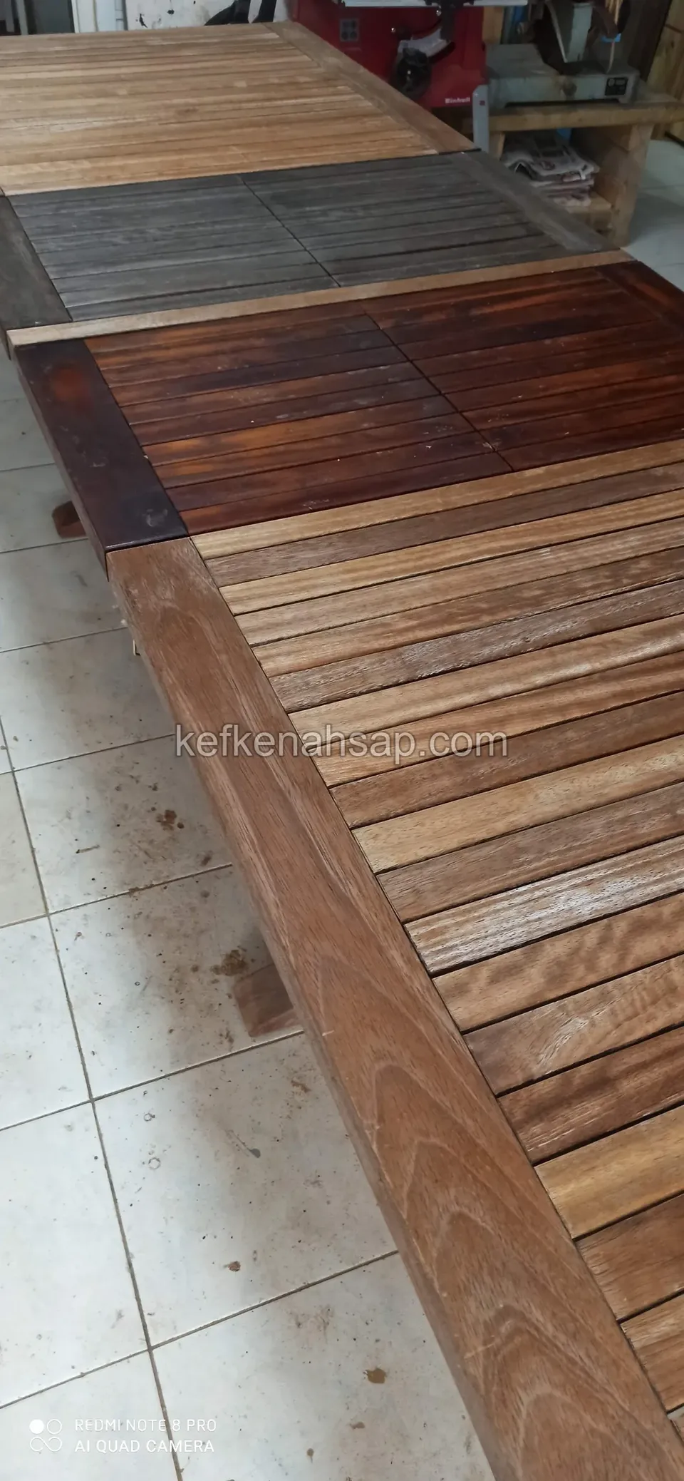 Auf Fliesenboden liegt die Lattenfläche einer langen Holztischplatte, ein Abschnitt ist dunkel behandelt