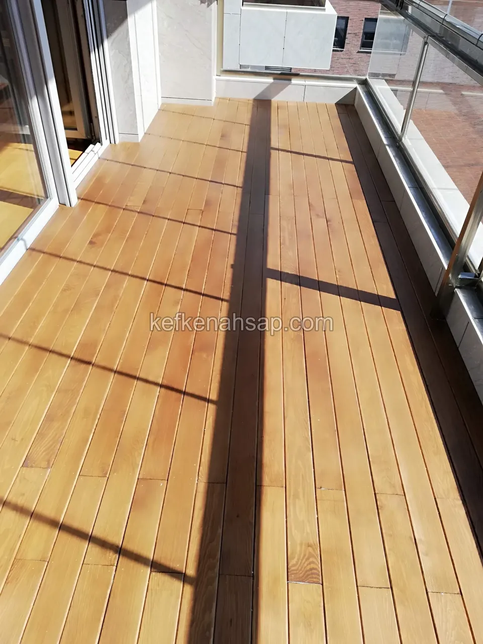 Light yellow timber decking on a long balcony along the glazed frame