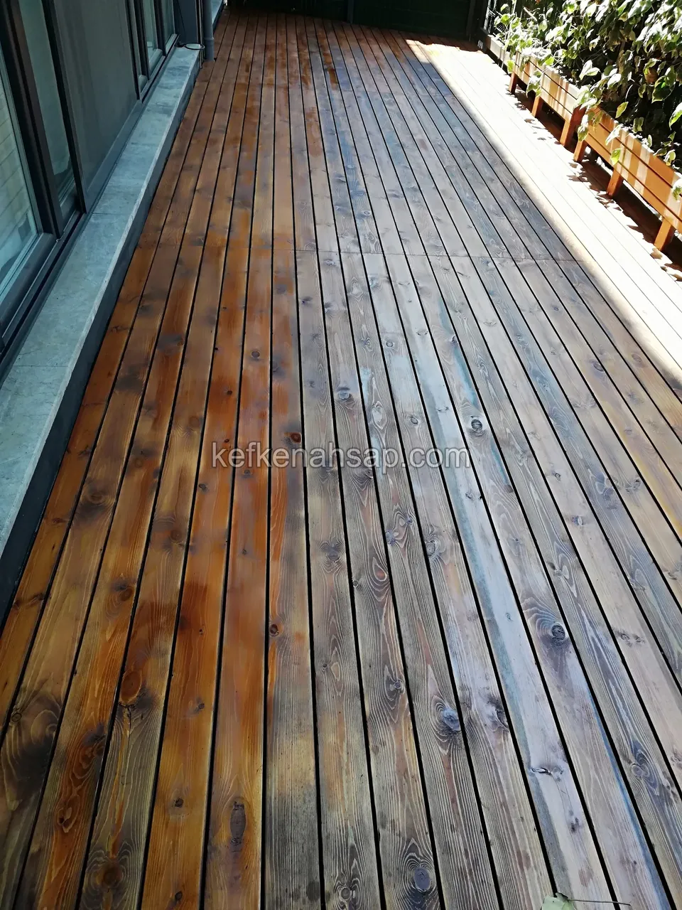 Deck boards on a long balcony, partly stained dark and partly wet and grey