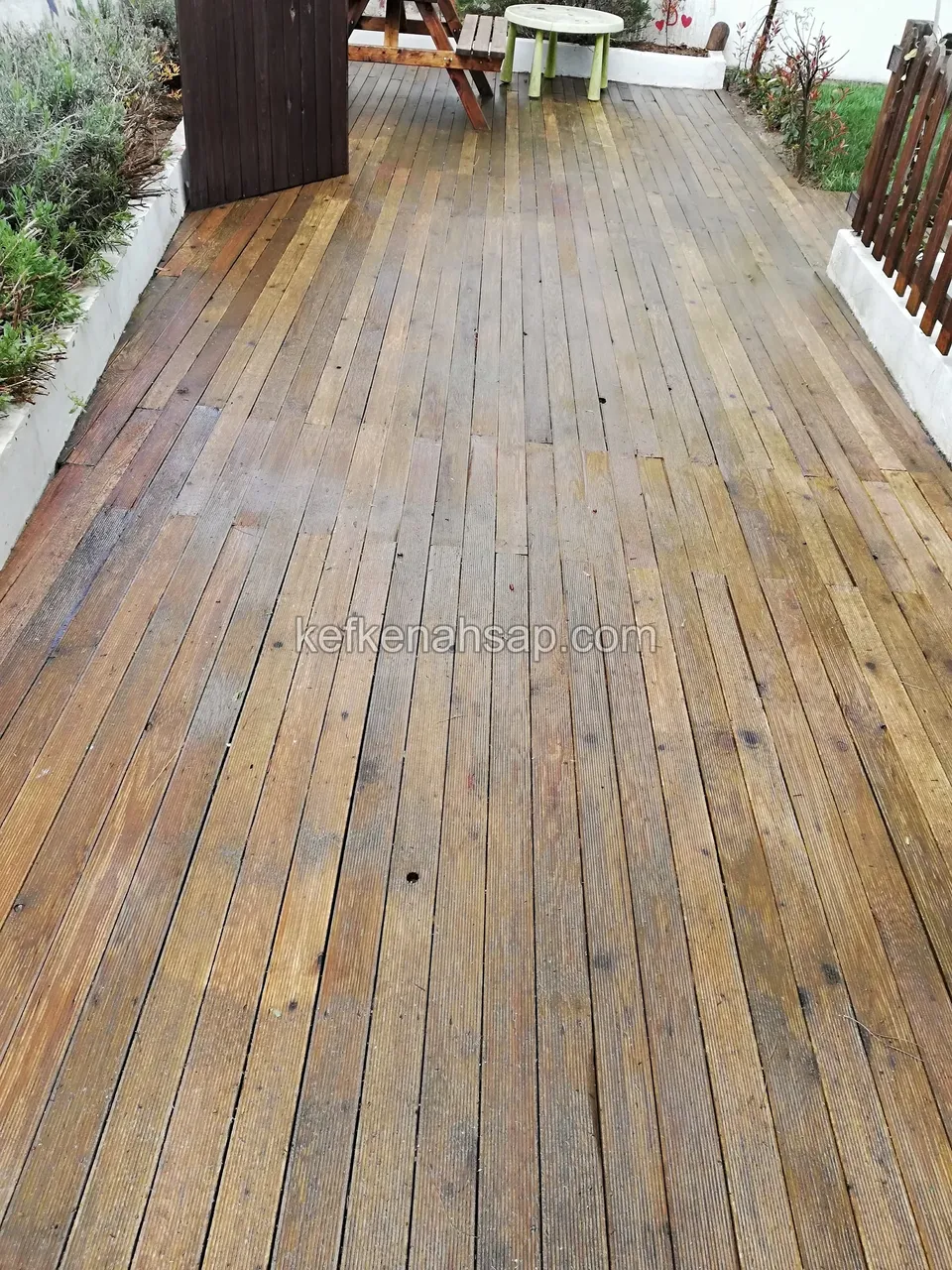 Uzun, ıslak görünümlü kahverengi ahşap deck zemini; kenarda çit ve masa
