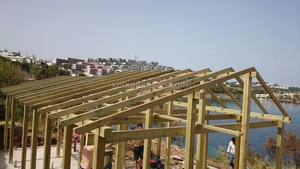 Uzun kamelyanın sık dizili çatı kirişleri, arkada deniz, kıyıdaki evler ve çalışan işçiler