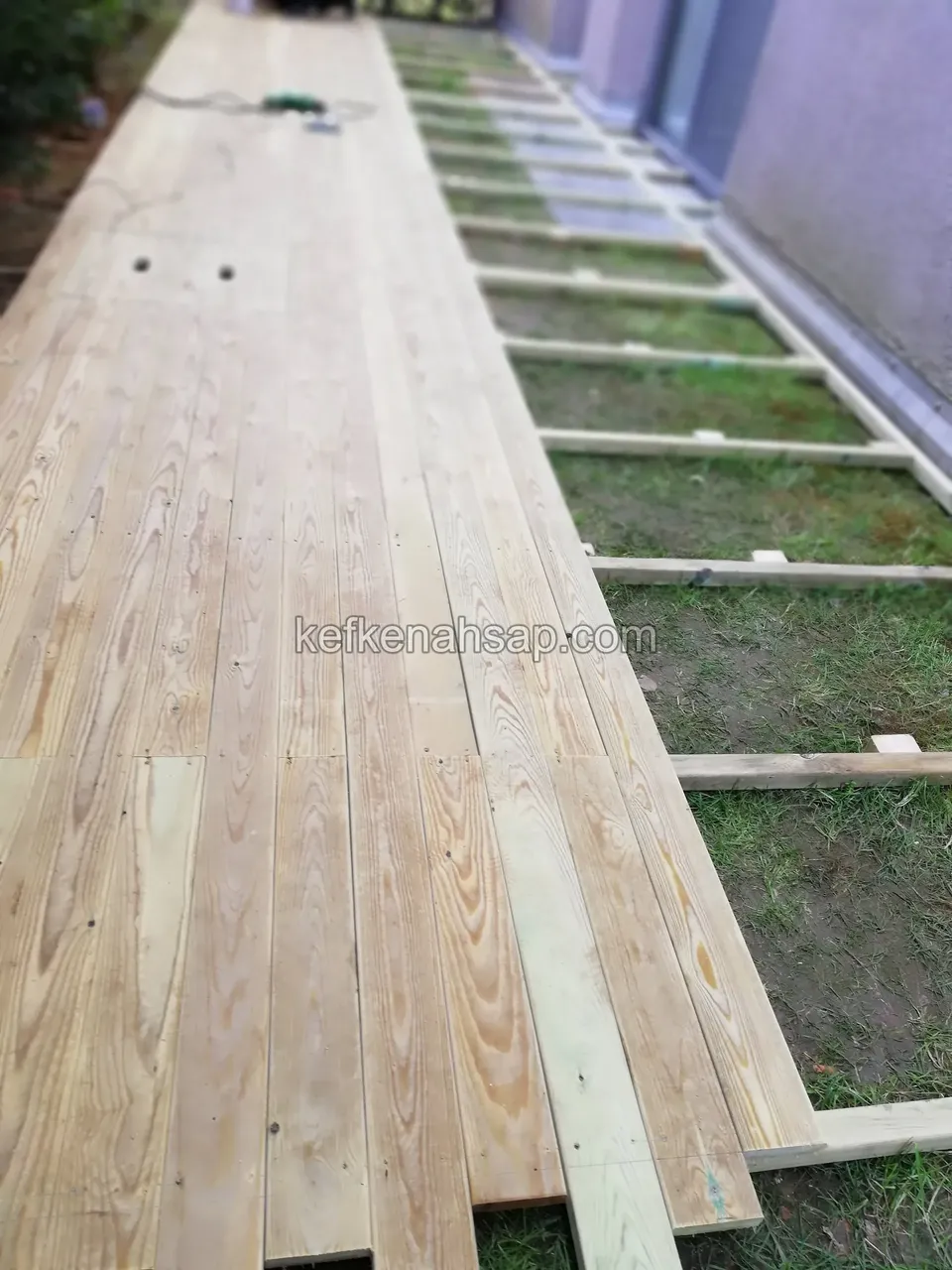 Deck boards being laid along a long side terrace, the remainder still on bare joists