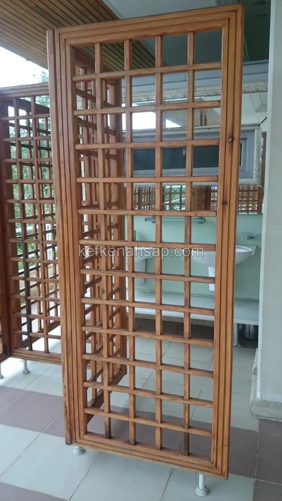 Verandada metal ayaklar üzerinde duran, kare kafes desenli ahşap bölme panelleri