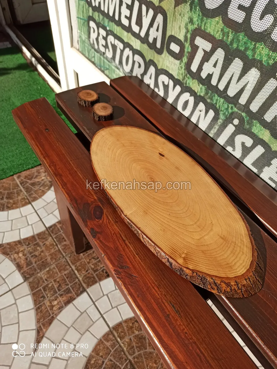 Auf einer dunkel lackierten Holzbank liegt eine große Baumscheibe mit Rindenrand und zwei kleine Scheiben