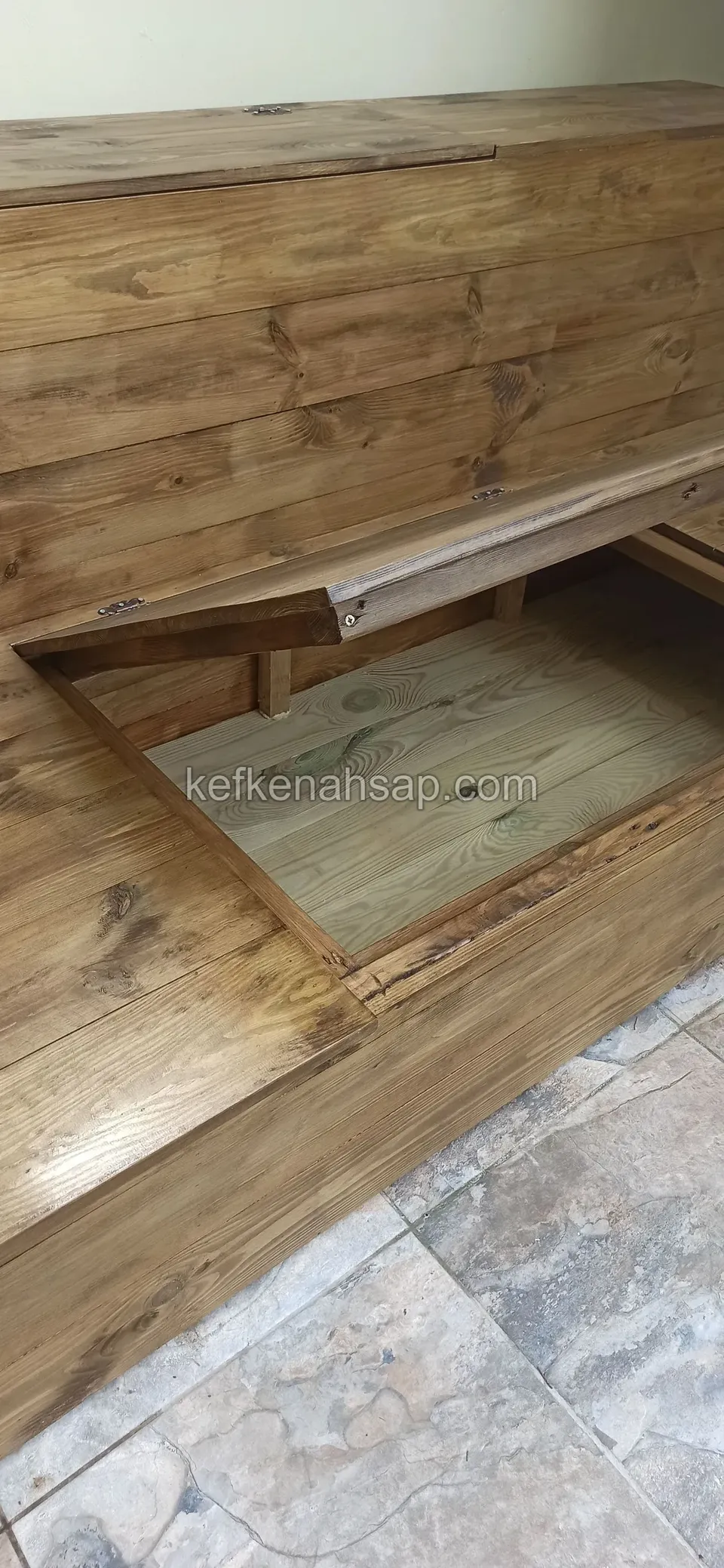 Eine lackierte Holzliege mit angelehntem Deckel, im Inneren das helle Staufach, die Seite aus Kiefernbrettern
