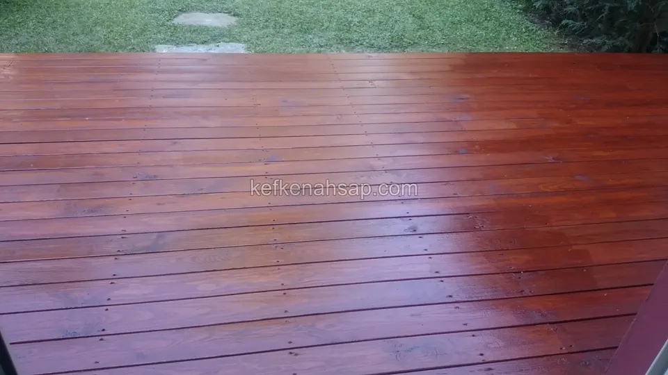 Koyu kırmızı kahve renkte cilalanmış deck yüzeyi, tahta aralarında düzgün vida sıraları ve üst kenarda çimen