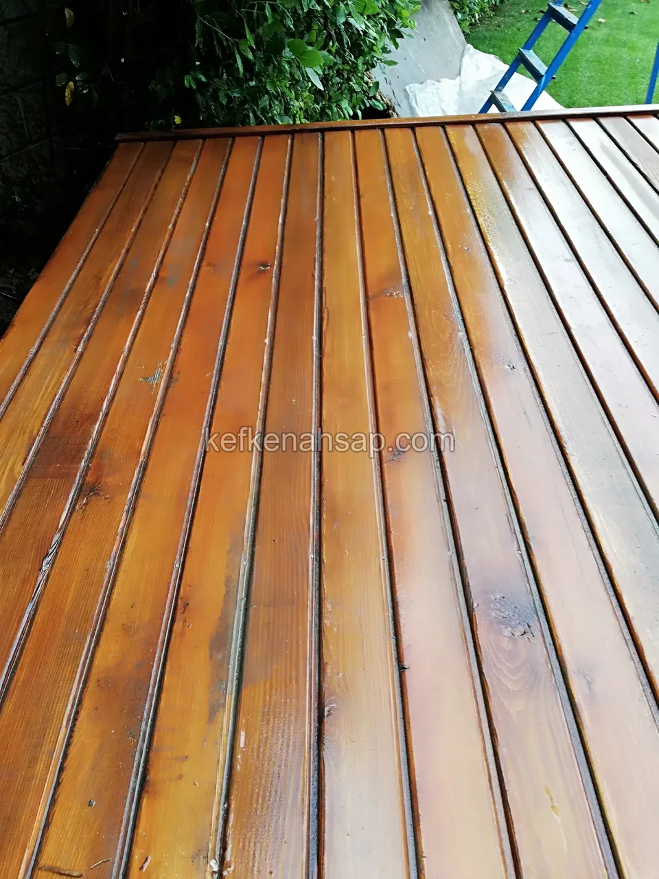 Nahaufnahme von mit orange getöntem Holzschutz behandelten Terrassendielen, die Kiefernmaserung ist zu sehen