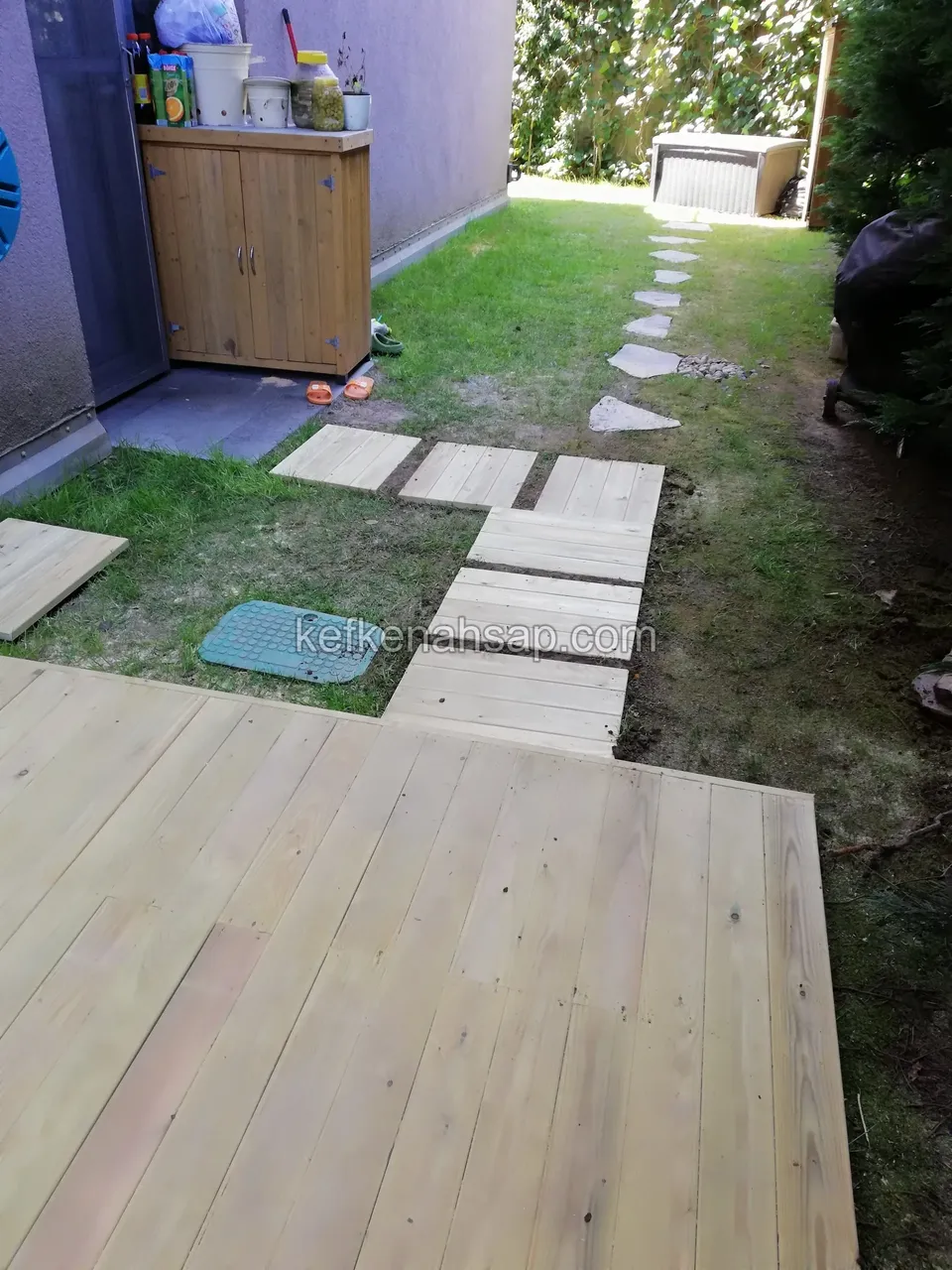 Yan bahçede deck ve devamında çimde sıralanan ahşap basamak tahtalarından yürüyüş yolu