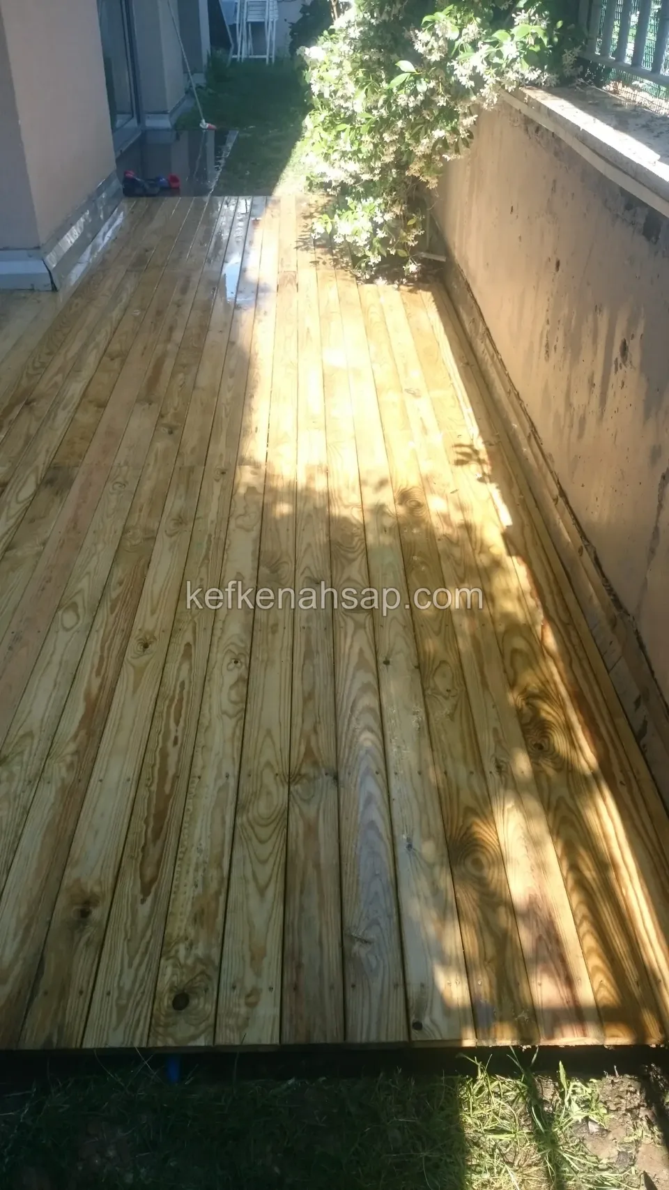 Newly laid timber deck running along a wall in a side garden, with sunlight on the boards