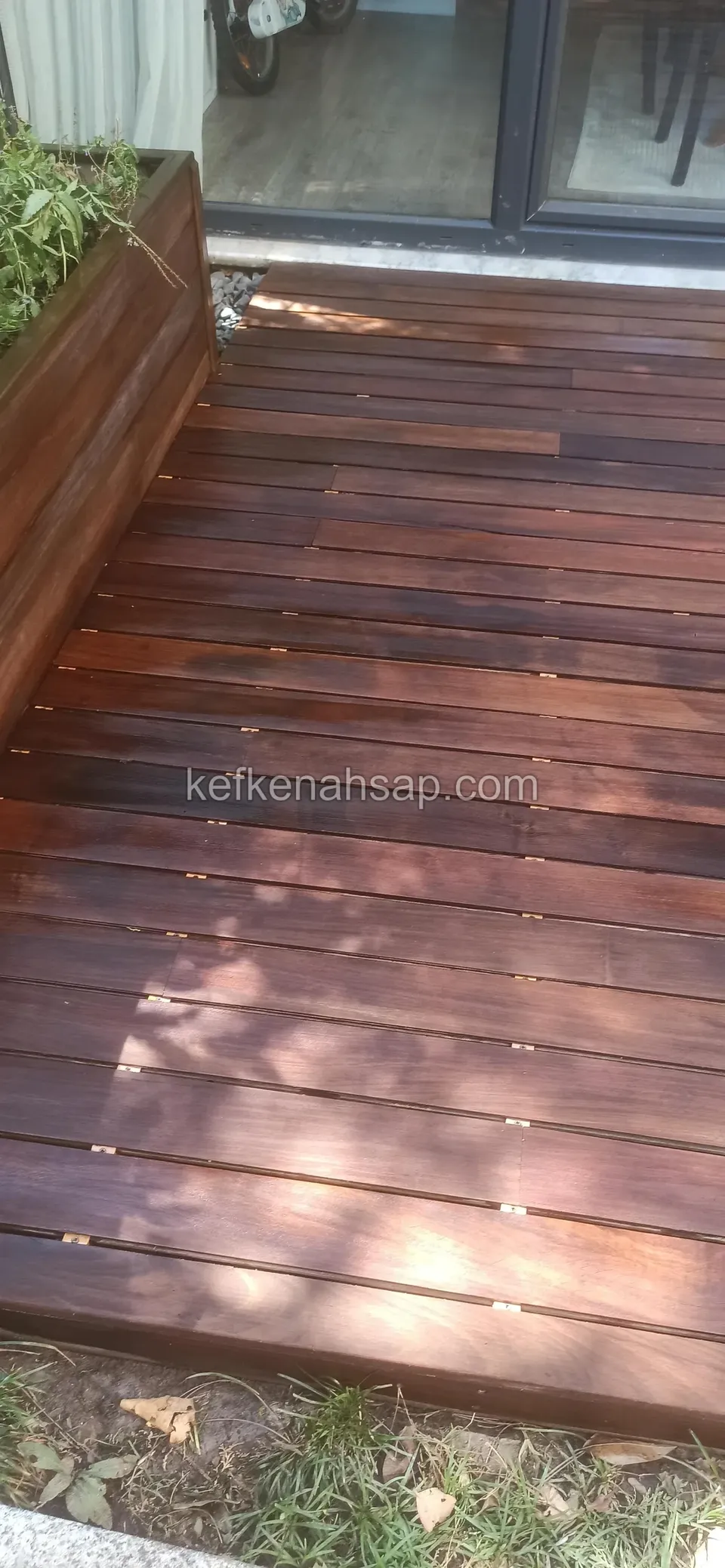Dark brown deck boards in front of a glass door with a timber planter set along one edge