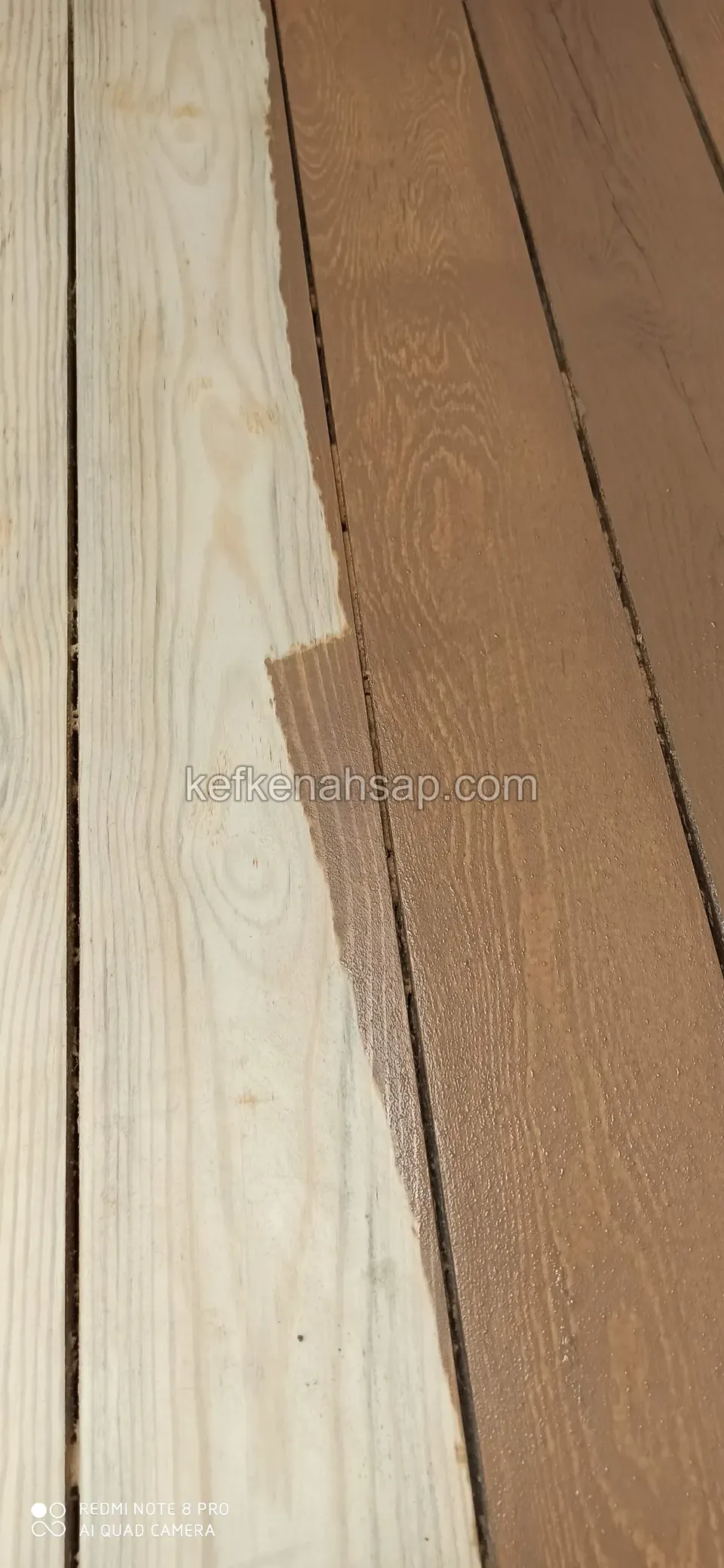 Blanke helle Kiefernbretter neben bereits braun gestrichenen, die Streichkante verläuft diagonal