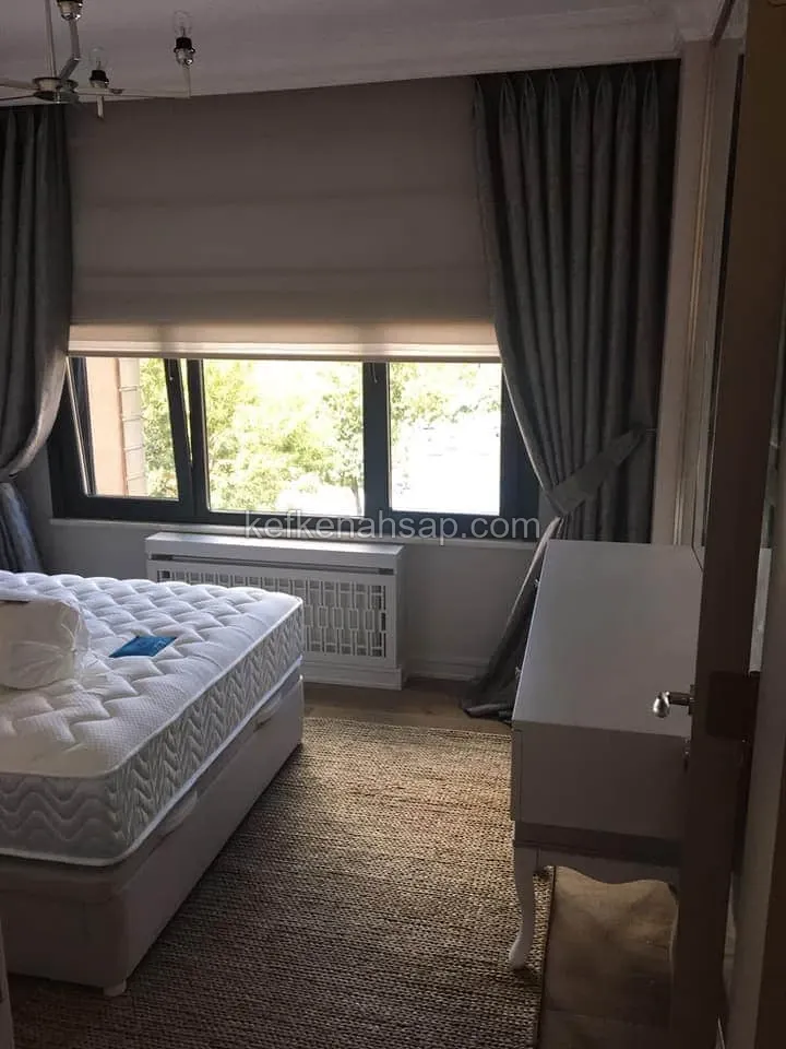 Yatak odası pencere altında beyaz petek kapağı ve sağda beyaz çekmeceli komodin.