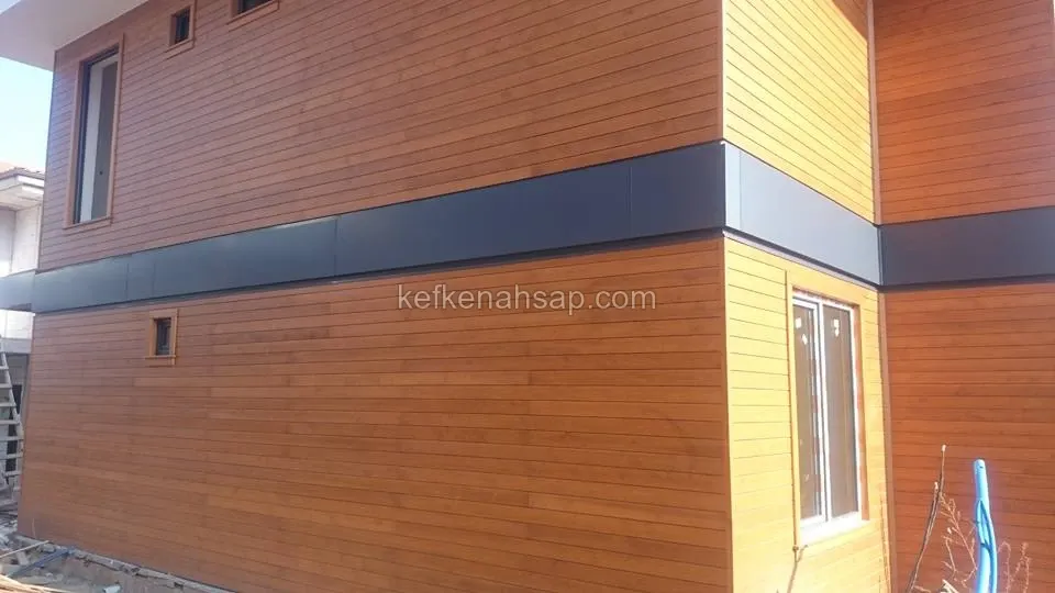 Yatay çıtalı ahşap kaplanmış iki katlı evin köşesi, katlar arasında koyu gri metal bant ve pencereler