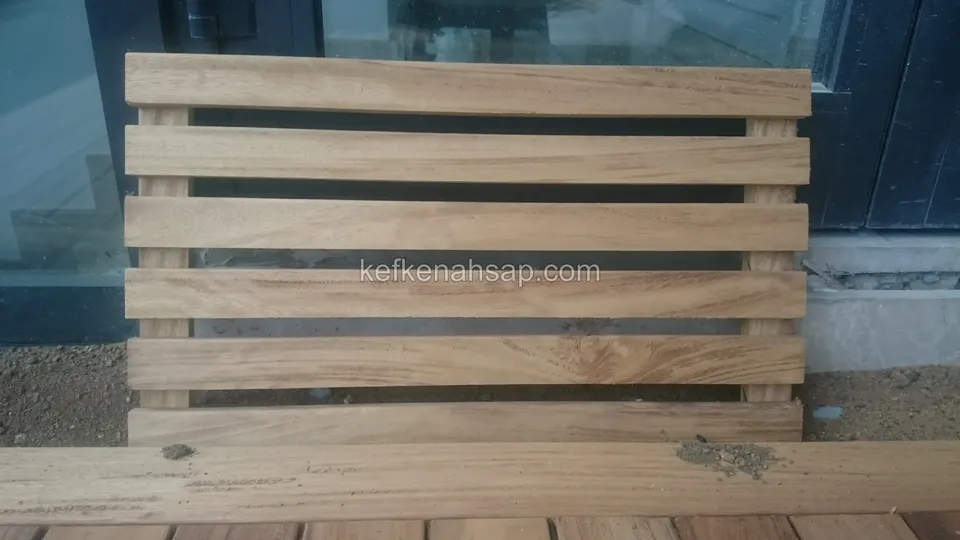 Cam önünde duran, aralıklı yatay çıtalı ve iki dikmeli küçük açık kahve ahşap panel; altta bir tahta parçası