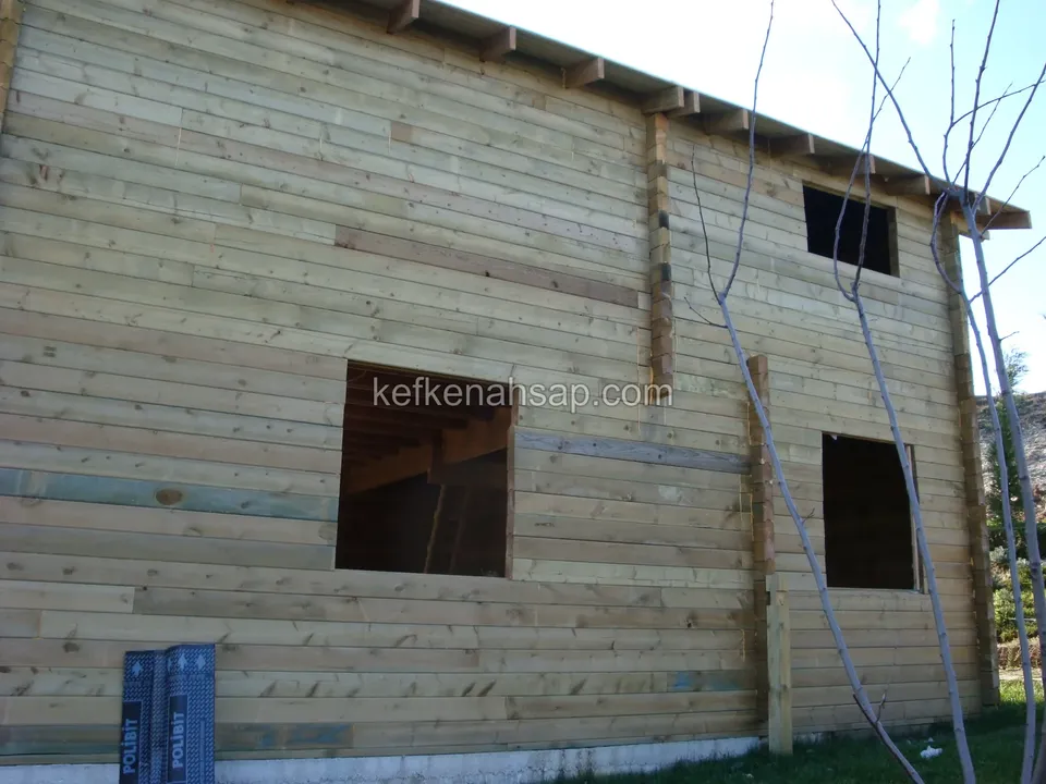 Pencere boşlukları henüz açık olan, yatay tahta kaplı yapım aşamasındaki ahşap ev cephesi