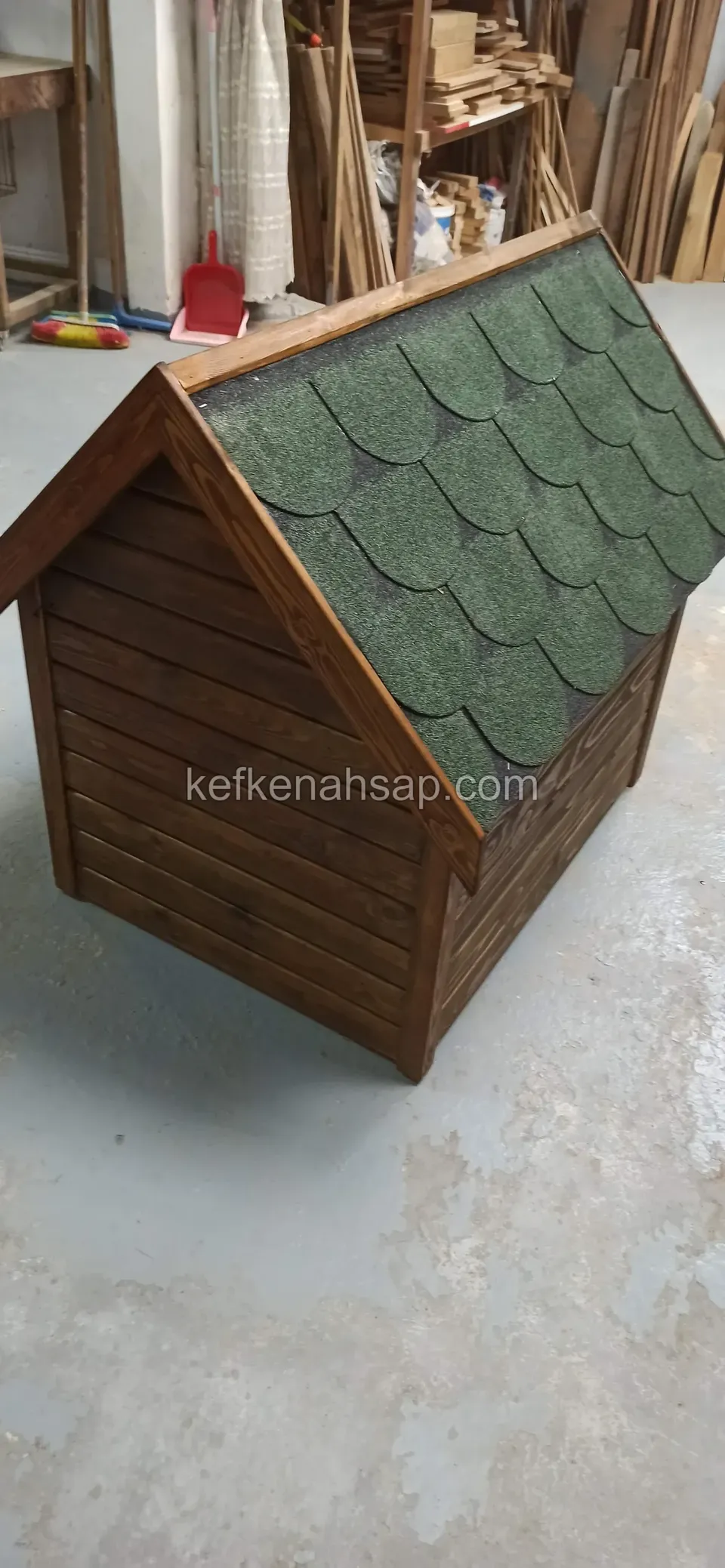 Yatay kaplamalı koyu vernikli köpek kulübesinin yeşil shingle çatılı yan yüzü