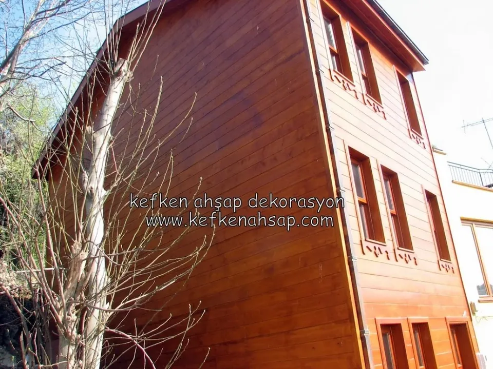 Yatay ahşap kaplamalı, kırmızımsı kahverengi vernikli üç katlı evin cephesi; pencere altlarında oyma süslemeler var.