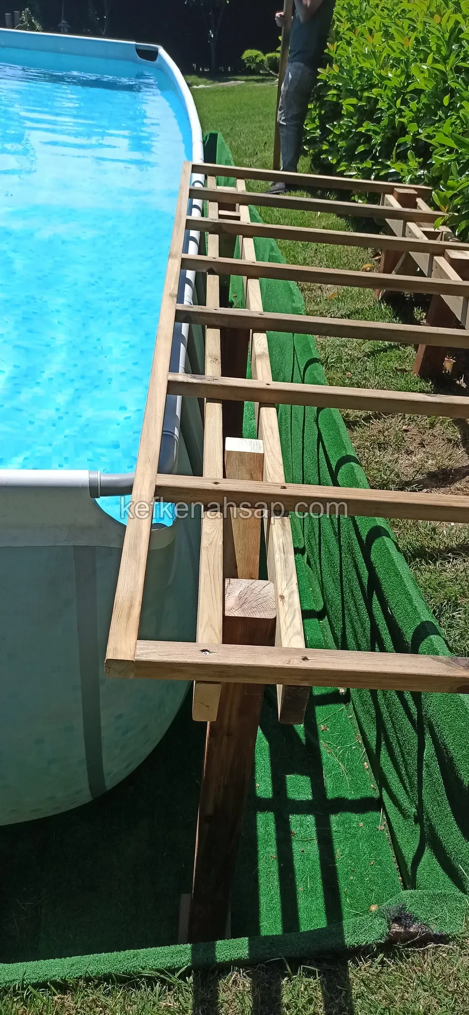 Timber support frame built beside an above-ground pool on green artificial turf
