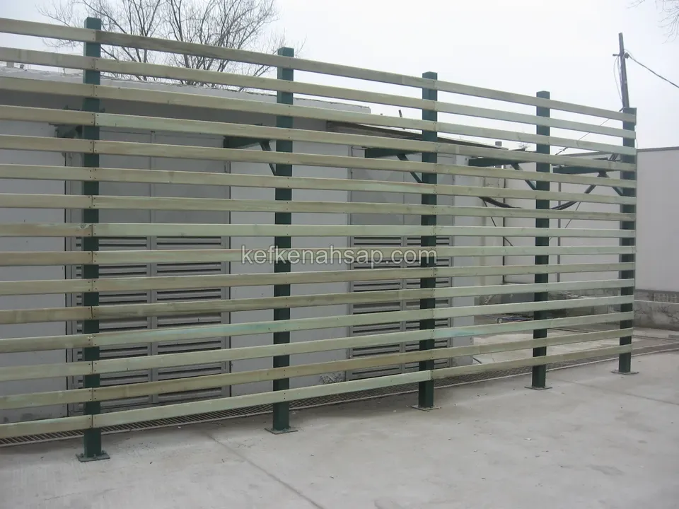 A long horizontal-slat timber fence fixed to green-painted metal posts on grey paving, with bare trees and sky behind