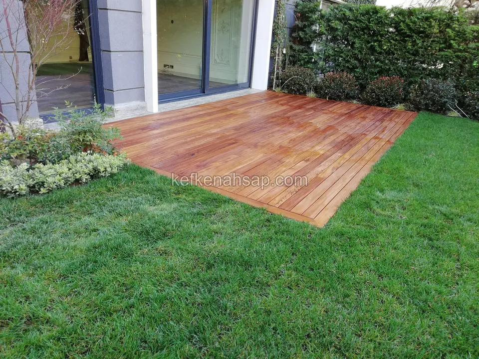 Reddish, oil-finished-looking timber deck surrounded by green lawn, with a building with glass doors behind