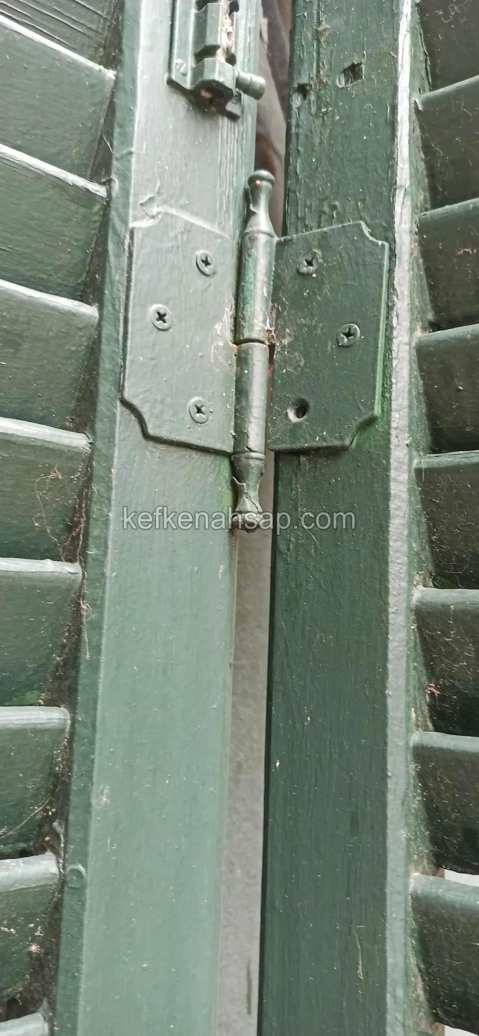 Yeşil boyalı, jaluzi çıtalı bir panjur kanadının dikme kısmında metal menteşe ve vida sıraları