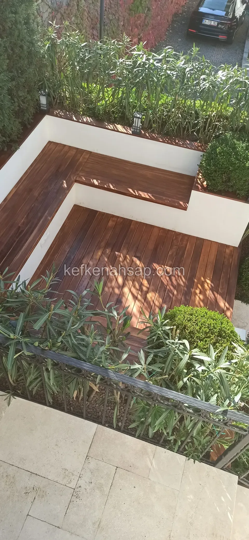 Aus erhöhter Perspektive: eine dunkel lackierte Holzbank und ein Terrassenboden, eingefasst von weiß verputzten Mauern