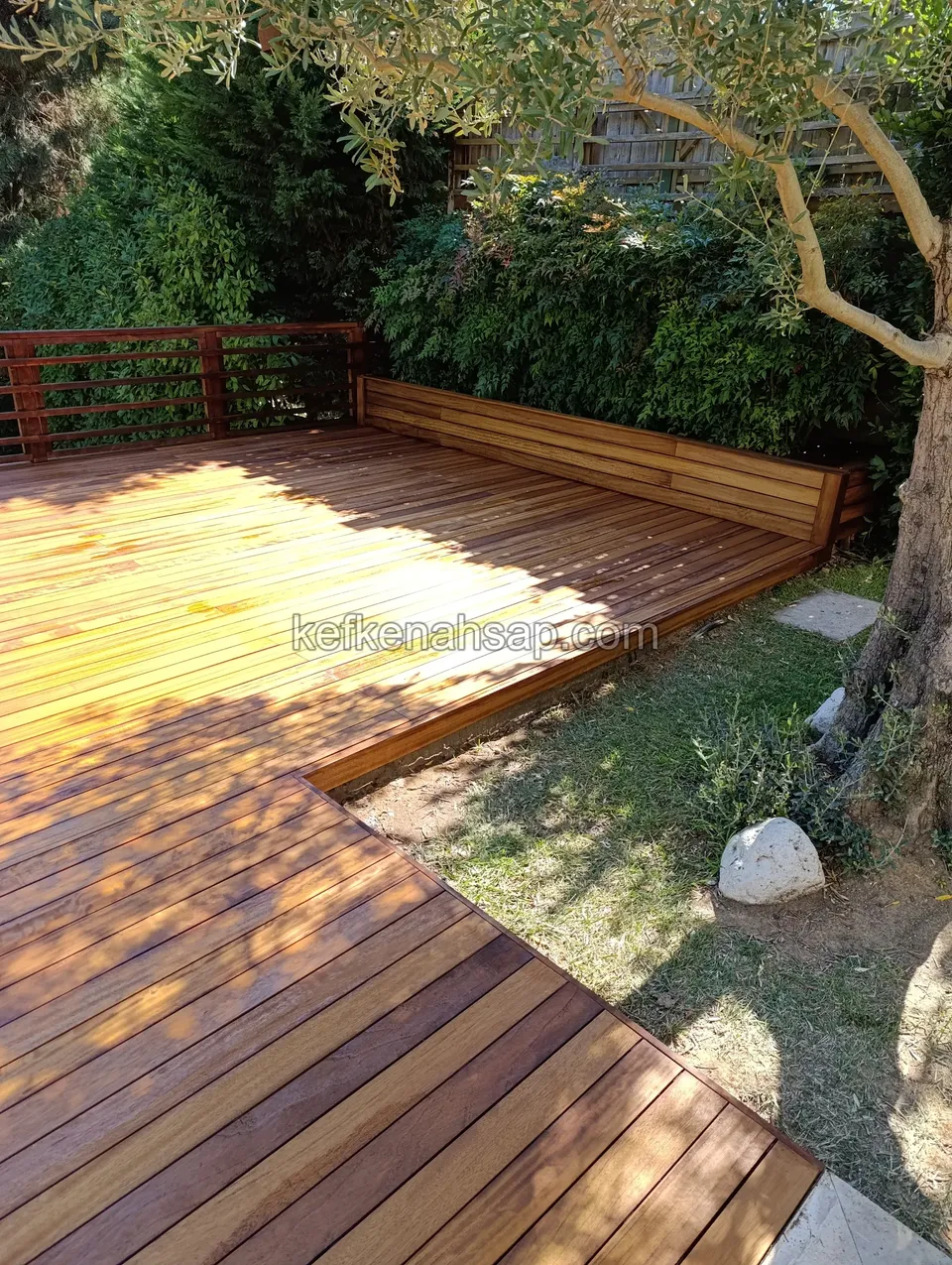 Deck stretching under an olive tree, with a railing behind and a seating box along the side wall