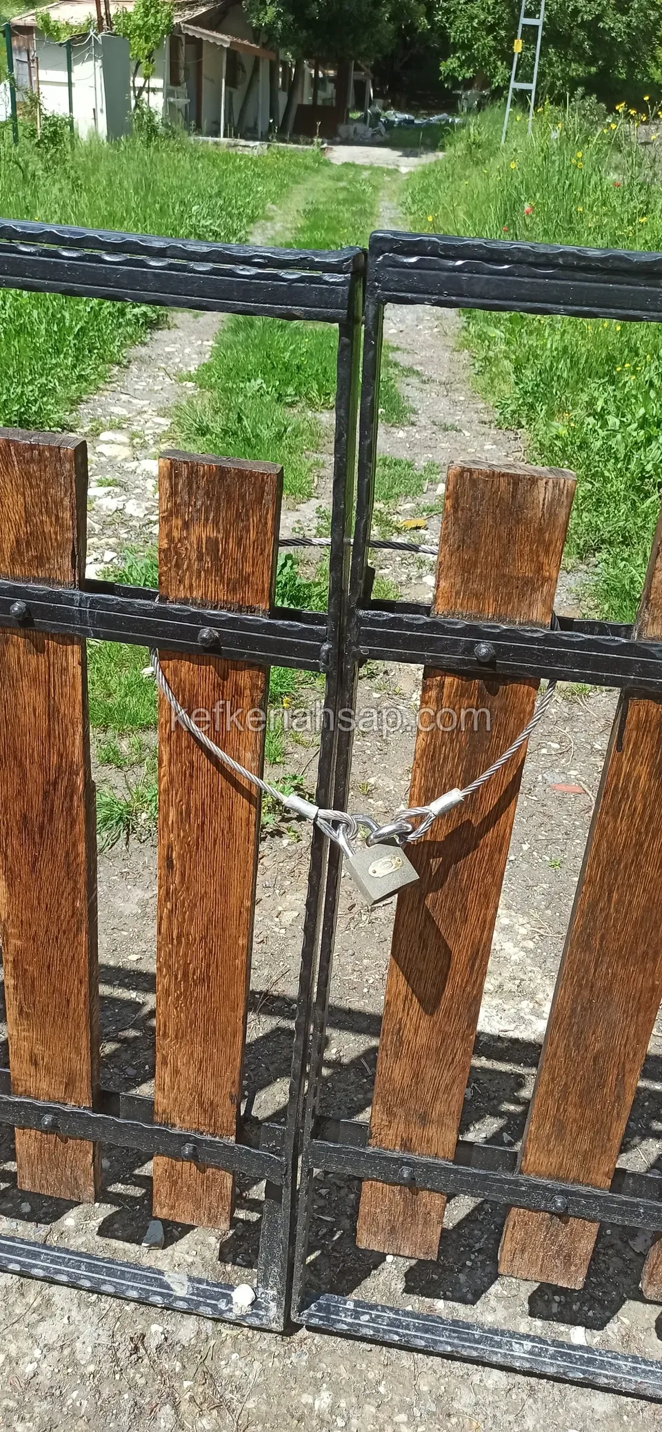 Metal çerçeveli çift kanatlı kapının birleşim yerinde zincir ve asma kilit, iki yanda kahverengi ahşap çıtalar